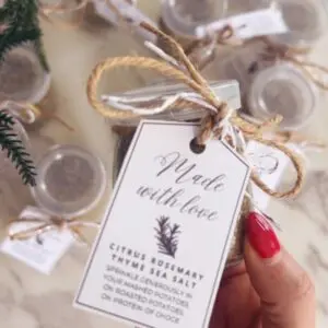 Four ingredients for citrus herb sea salt including dried orange slices, fresh rosemary, thyme, and celtic sea salt on white surface