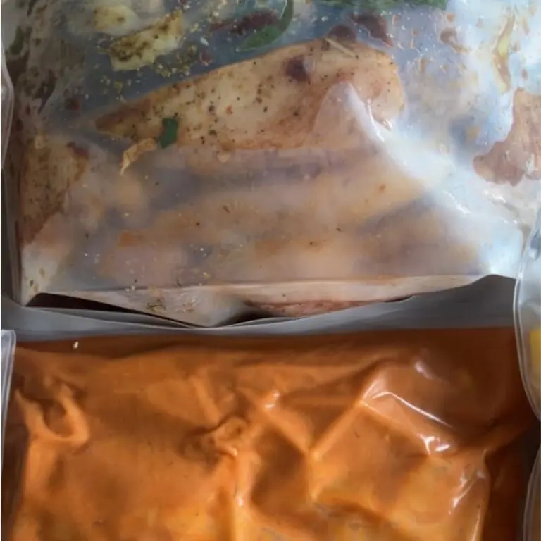Four labeled reusable freezer bags filled with prepared ingredients for Tuscan Chicken, Butter Chicken, Beef Stroganoff, and Farmer's Sausage Bowls freezer meals