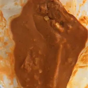 Reusable freezer bag with layered butter chicken ingredients: cubed chicken, diced onions, tomatoes, coconut milk, and spices ready to freeze