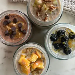 Four mason jars filled with overnight oats in four different flavors, each labeled with the flavor name and topped with fresh fruit and toppings.