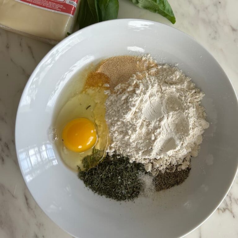 Bowl of smooth cottage cheese, ground chia seeds, almond flour, and spices arranged on white marble countertop for pizza crust preparation