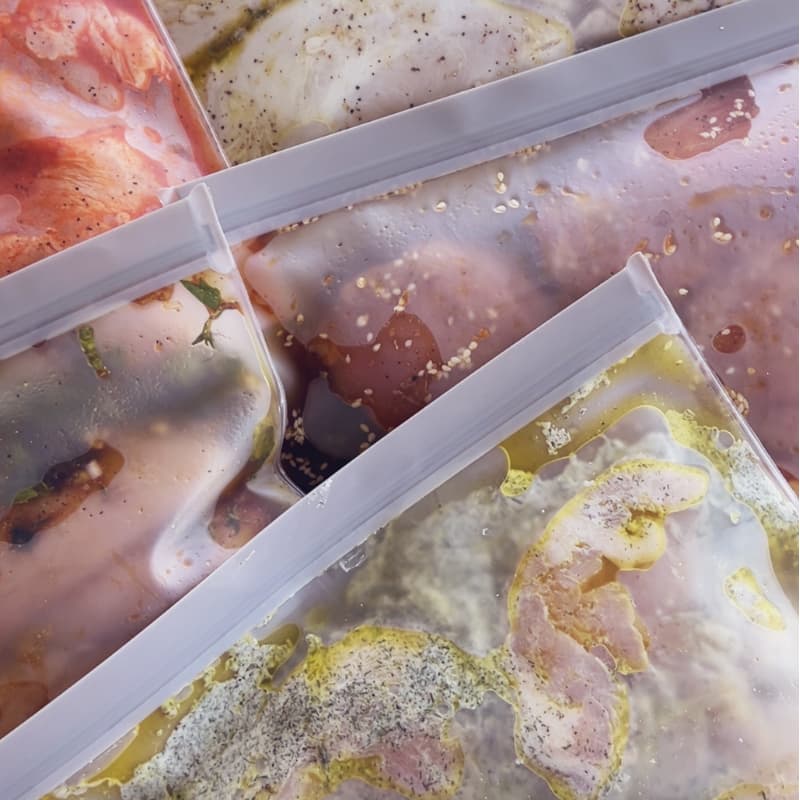 Five labeled freezer bags filled with different chicken marinades ready to freeze for meal prep