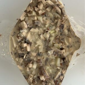 Reusable freezer bag filled with layered beef stroganoff ingredients: beef pieces, mushrooms, onions, and yogurt-based sauce ingredients ready for freezing